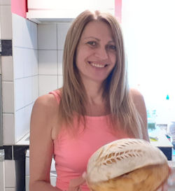 Szatmári Erika egy gyöyörű kenyeret tart a kezében, és mosolyog. Ezt a fotót egy nyomtatott újság számára készítettük, amikor interjút közöltek vele.